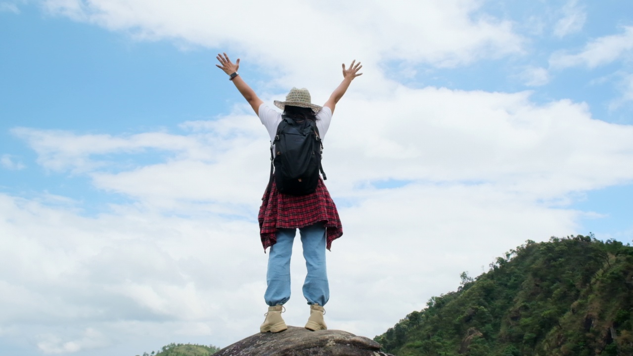 女背包客站在山顶，高举双臂，欣赏风景。旅程与成功理念视频素材