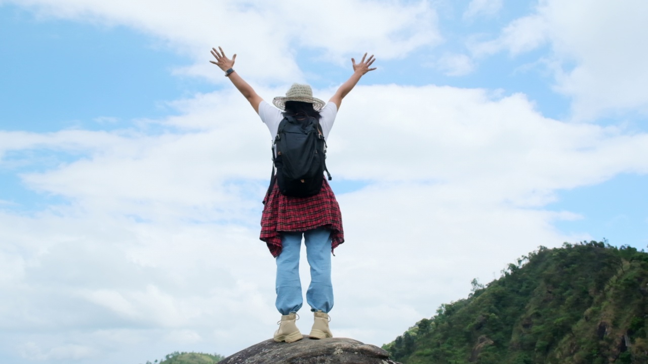 女背包客站在山顶，高举双臂，欣赏风景。旅程与成功理念视频素材