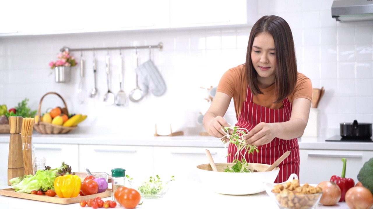 健康的生活方式和饮食观念。在厨房里搅拌新鲜沙拉的女人。年轻女子将葵花籽撒在沙拉碗上。视频素材