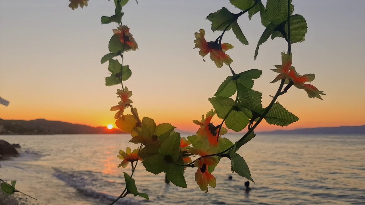 夏日的希腊，夕阳下的鲜花和在卡拉莫斯游泳的人们。视频素材