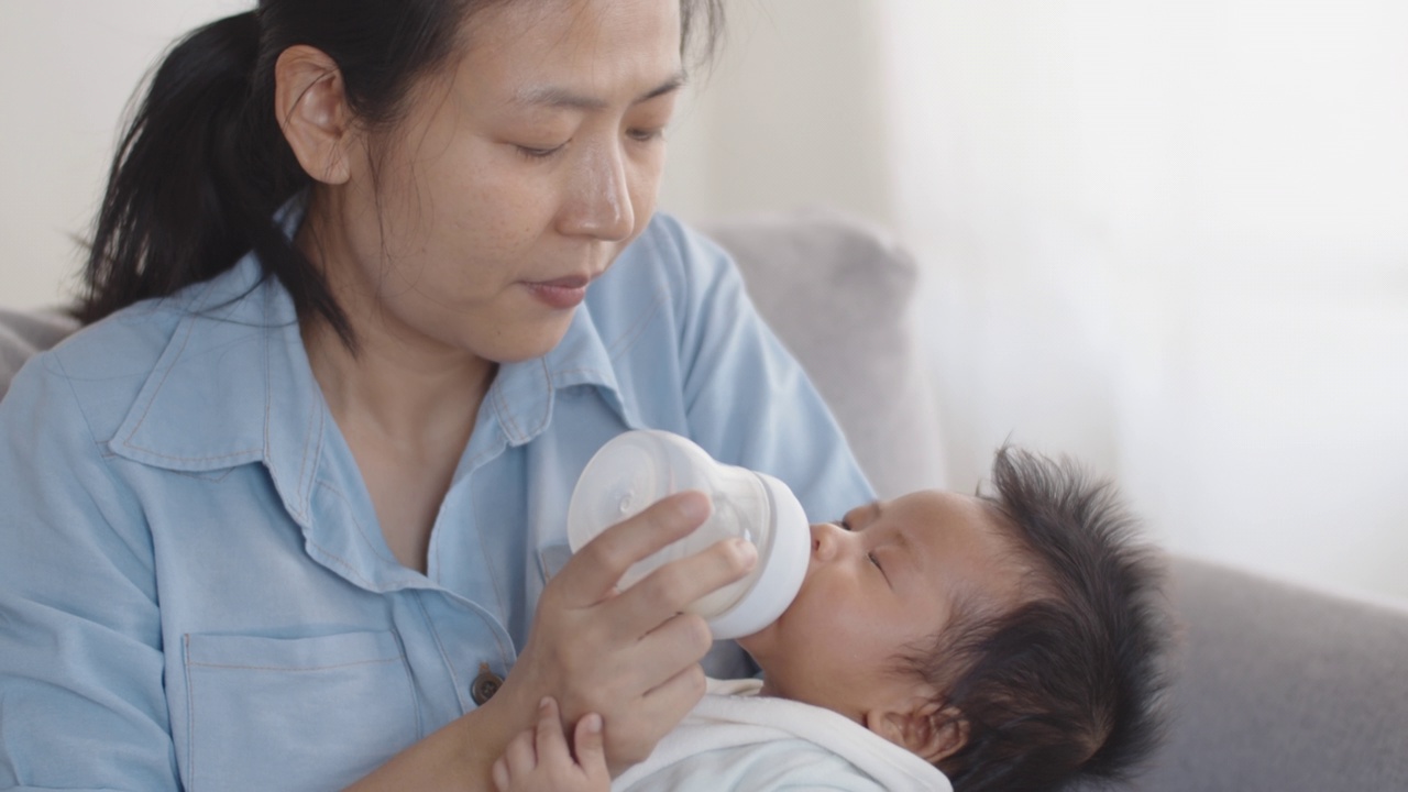 亚洲母亲用奶瓶喂她的新生婴儿在她的怀里。视频素材