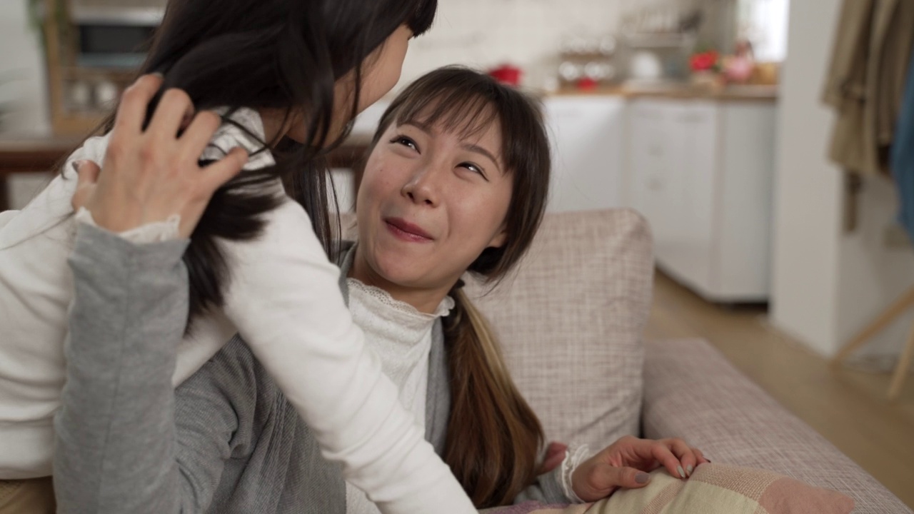 温柔的亚洲女儿在家里的沙发上拥抱和亲吻她的母亲。那个女人拍着那个女孩，微笑着称赞她视频素材