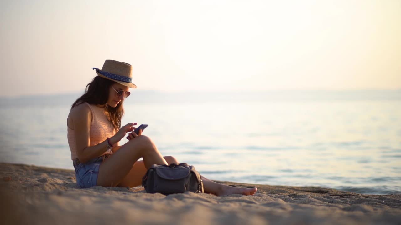 在海滩上用智能手机发短信的女人视频素材