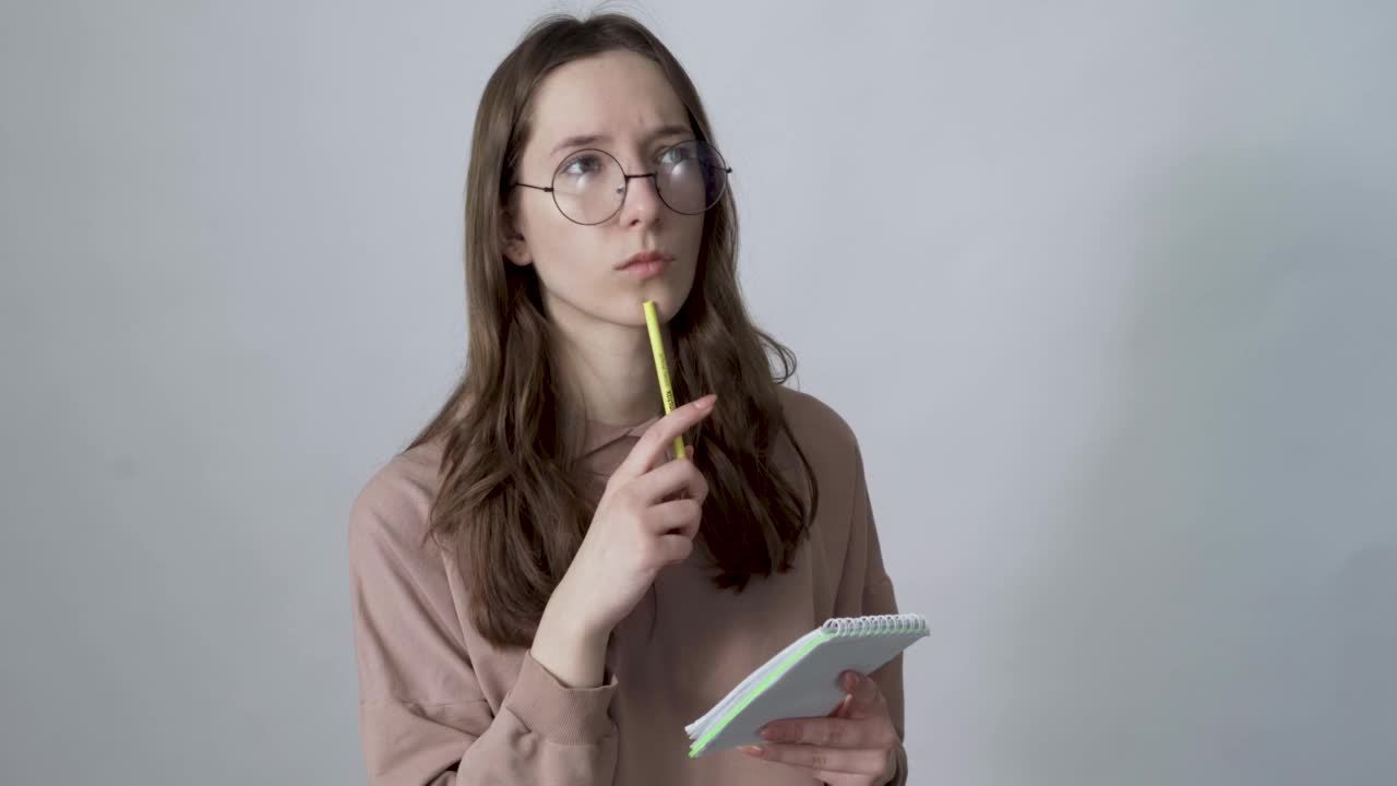 年轻的女子沉思着，在纸笔记本上做着笔记视频素材