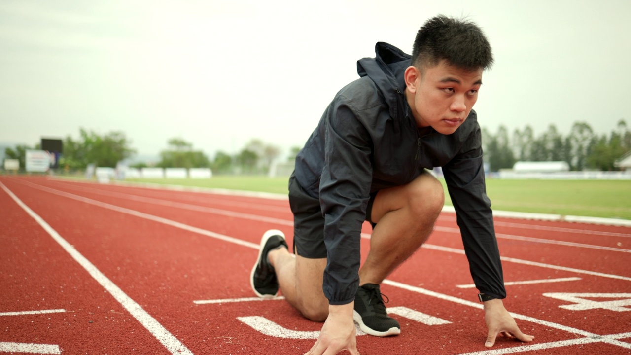 年轻英俊的中国男子在体育场跑道上跑步前摆明星姿势。挑战赛跑的运动员在起跑点奔跑。视频素材