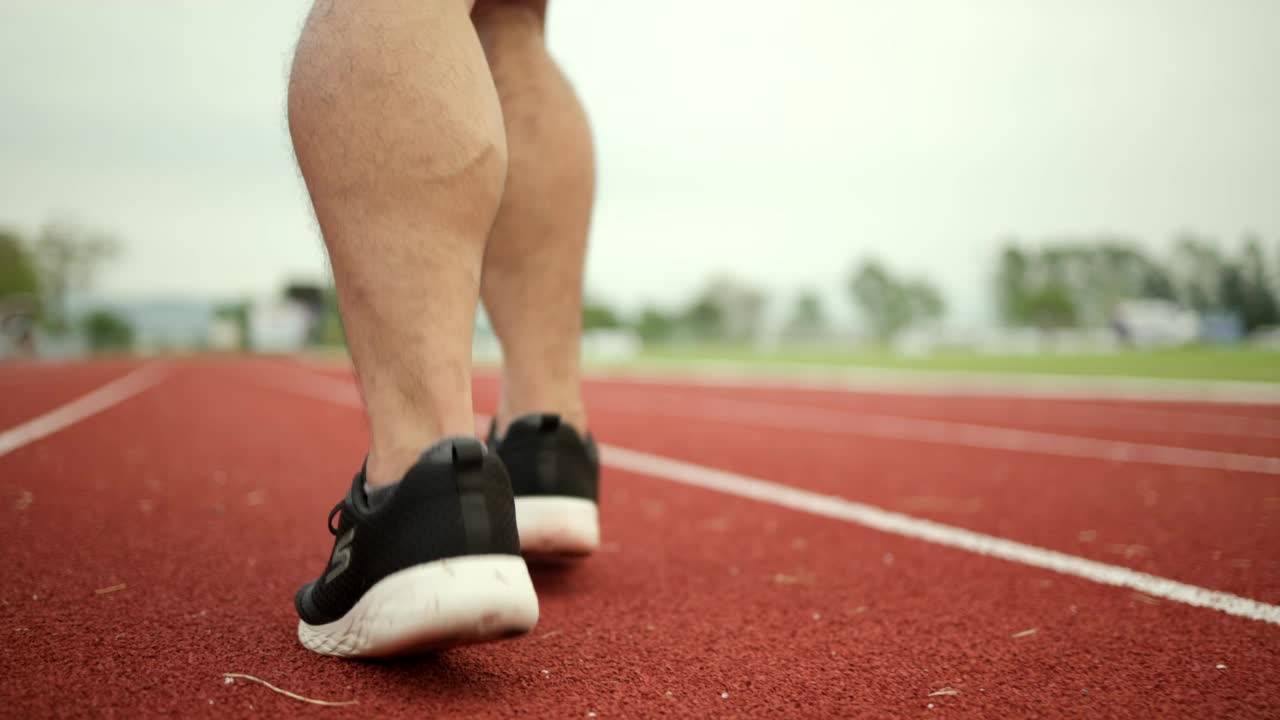 中国年轻男子穿着运动服在体育场跑道上跑步。健身男子在户外慢跑越过终点线。早上锻炼。健康积极的生活方式理念。视频素材