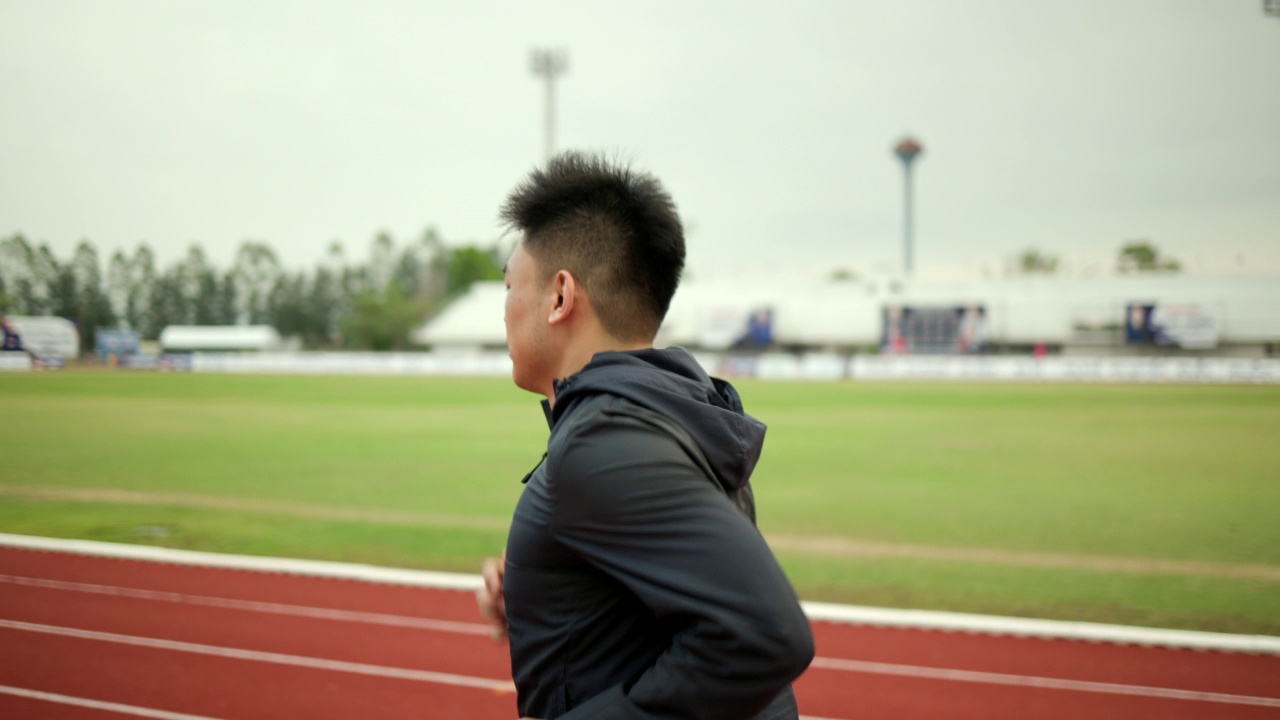 有魅力的年轻中国男子穿着运动服在体育场的跑道上跑步。健身男子在户外慢跑越过终点线。早上锻炼。健康积极的生活方式理念。视频素材