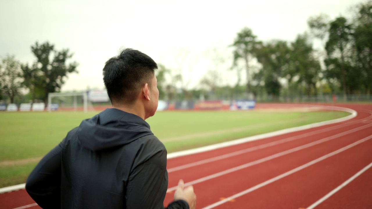 有魅力的年轻中国男子穿着运动服在体育场的跑道上跑步。健身男子在户外慢跑越过终点线。早上锻炼。健康积极的生活方式理念。视频素材