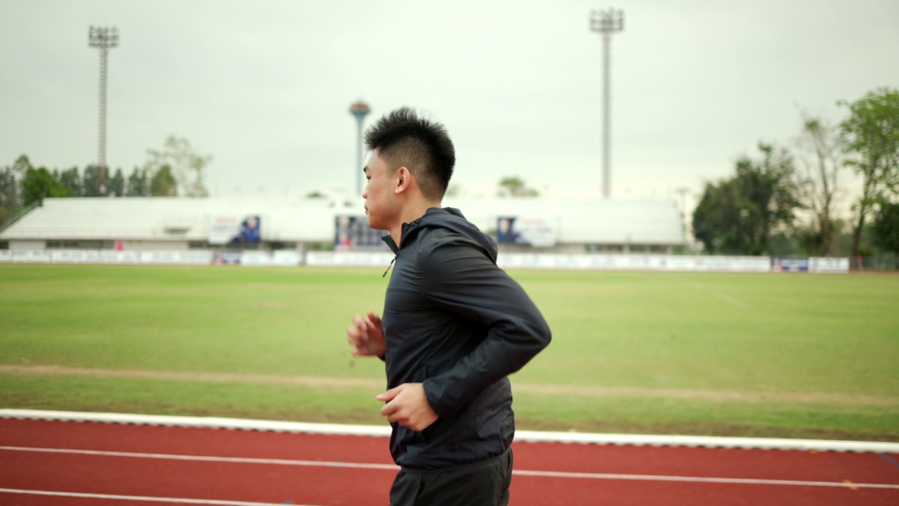 有魅力的年轻中国男子穿着运动服在体育场的跑道上跑步。健身男子在户外慢跑越过终点线。早上锻炼。健康积极的生活方式理念。视频素材