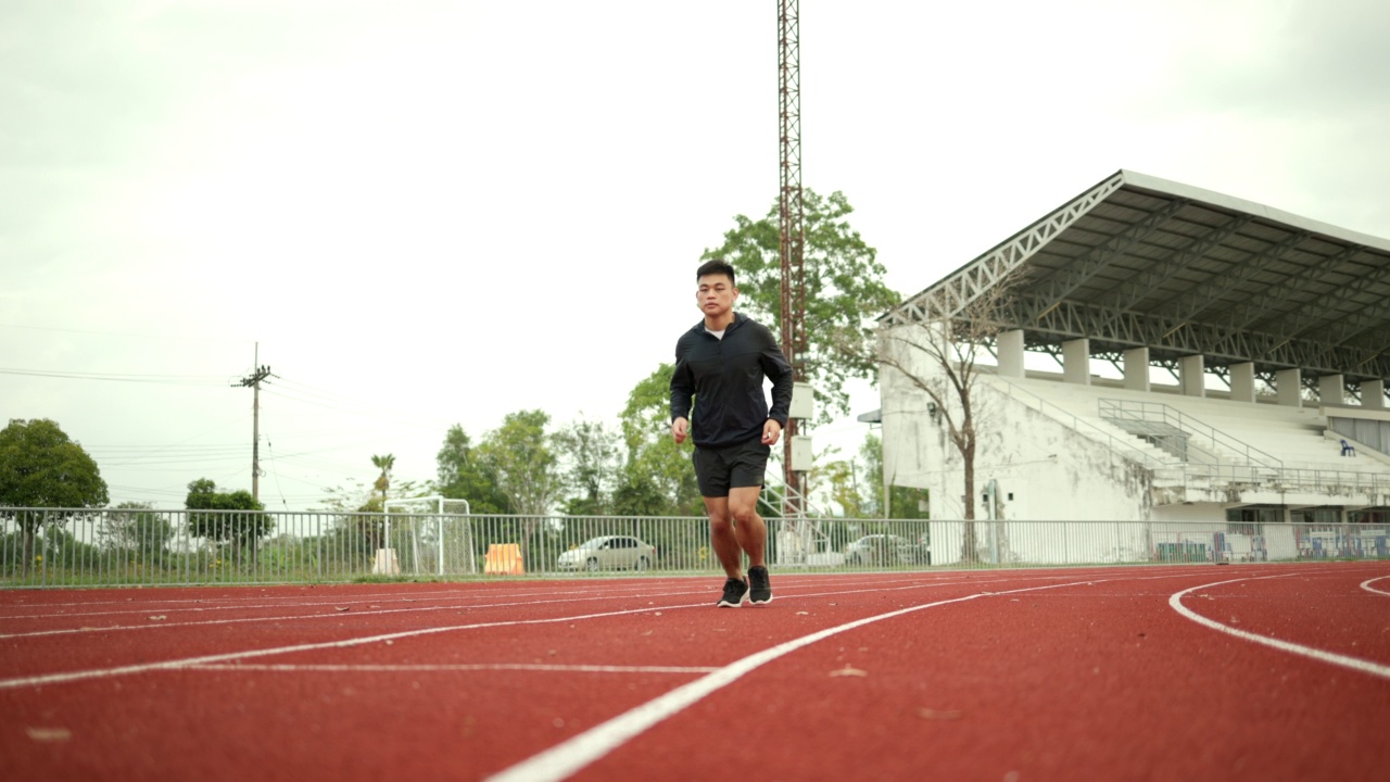 有魅力的年轻中国男子穿着运动服在体育场的跑道上跑步。健身男子在户外慢跑越过终点线。早上锻炼。健康积极的生活方式理念。视频素材