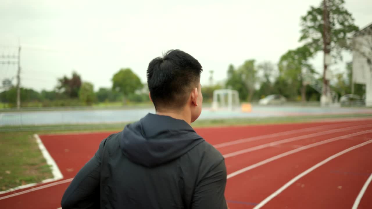 背部有吸引力的年轻男子穿着运动服在跑道上运行在体育场馆。健身男子在户外慢跑越过终点线。早上锻炼。健康积极的生活方式理念。视频素材