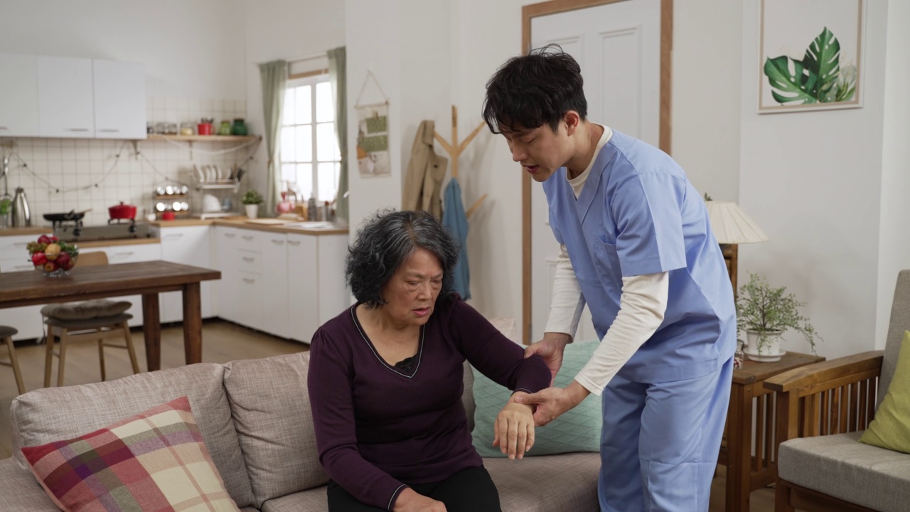 台湾私人护理人员在一位退休女性家中提供物理治疗支持。当她痛苦地呻吟时，他举起了她受伤的手臂视频素材