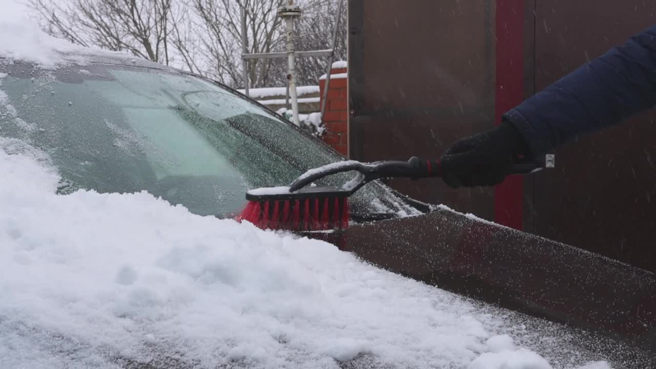 汽车在雪堆的特写。冬天的一天，一个穿深色夹克的男人在刷一辆车。视频素材