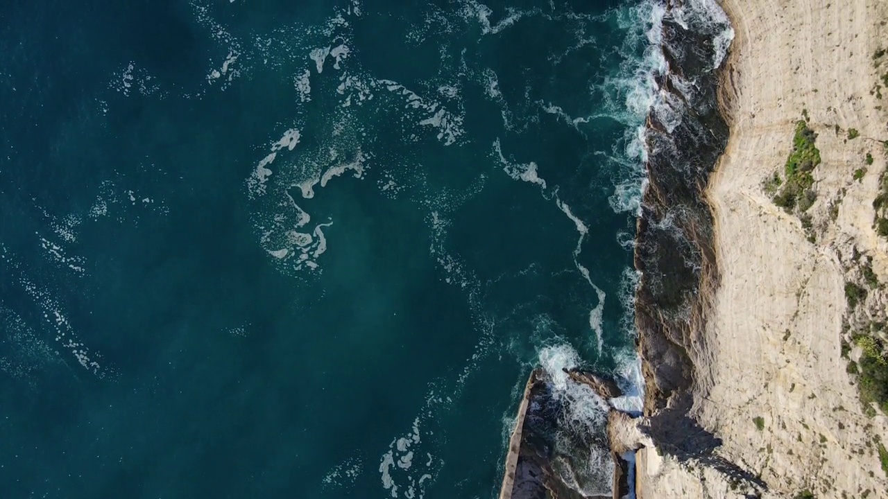 从空中俯瞰，海浪拍打着蓝色海洋中的岩石。海浪在美丽的海滩鸟瞰图无人机。从上方鸟瞰海浪撞击空岩悬崖的景象。视频素材