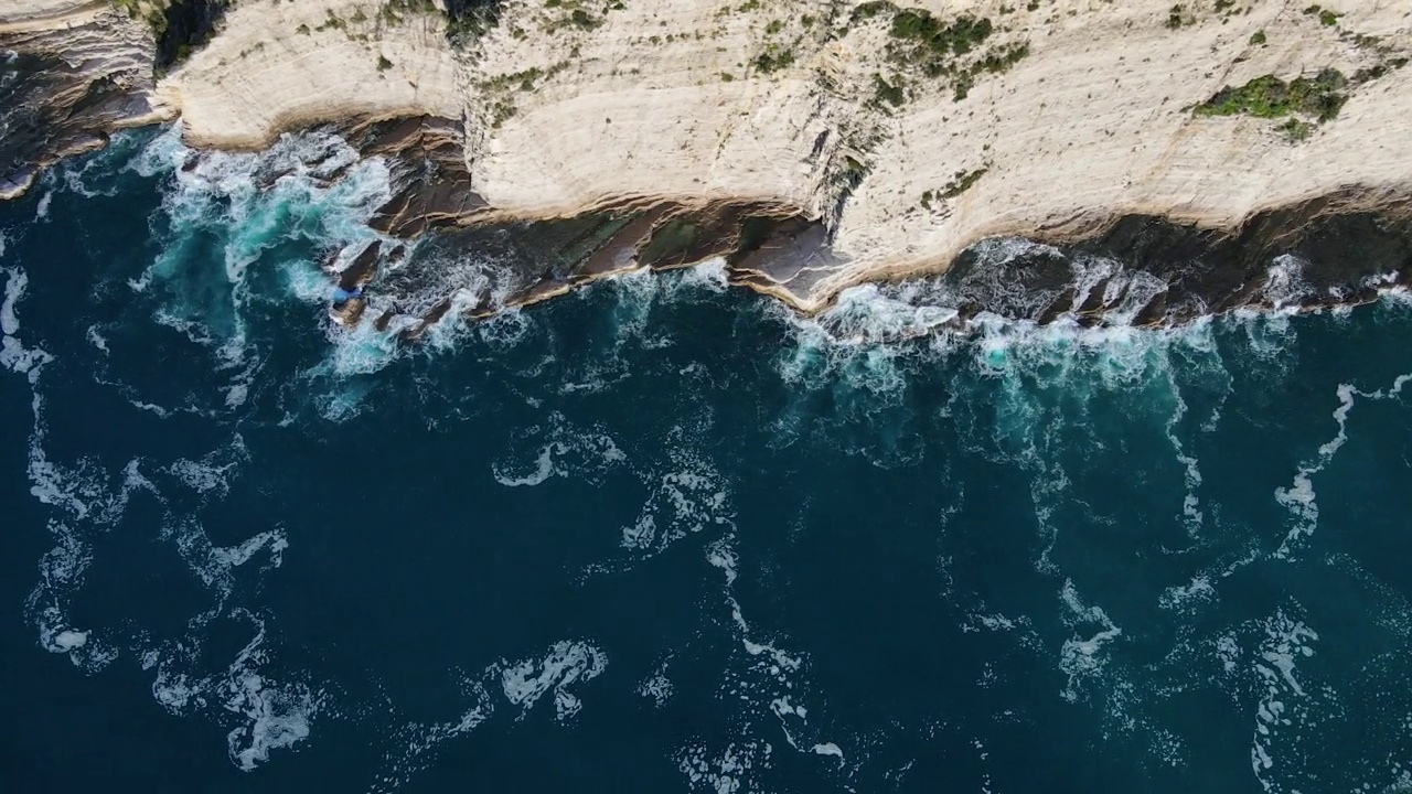 从空中俯瞰，海浪拍打着蓝色海洋中的岩石。海浪在美丽的海滩鸟瞰图无人机。从上方鸟瞰海浪撞击空岩悬崖的景象。视频素材