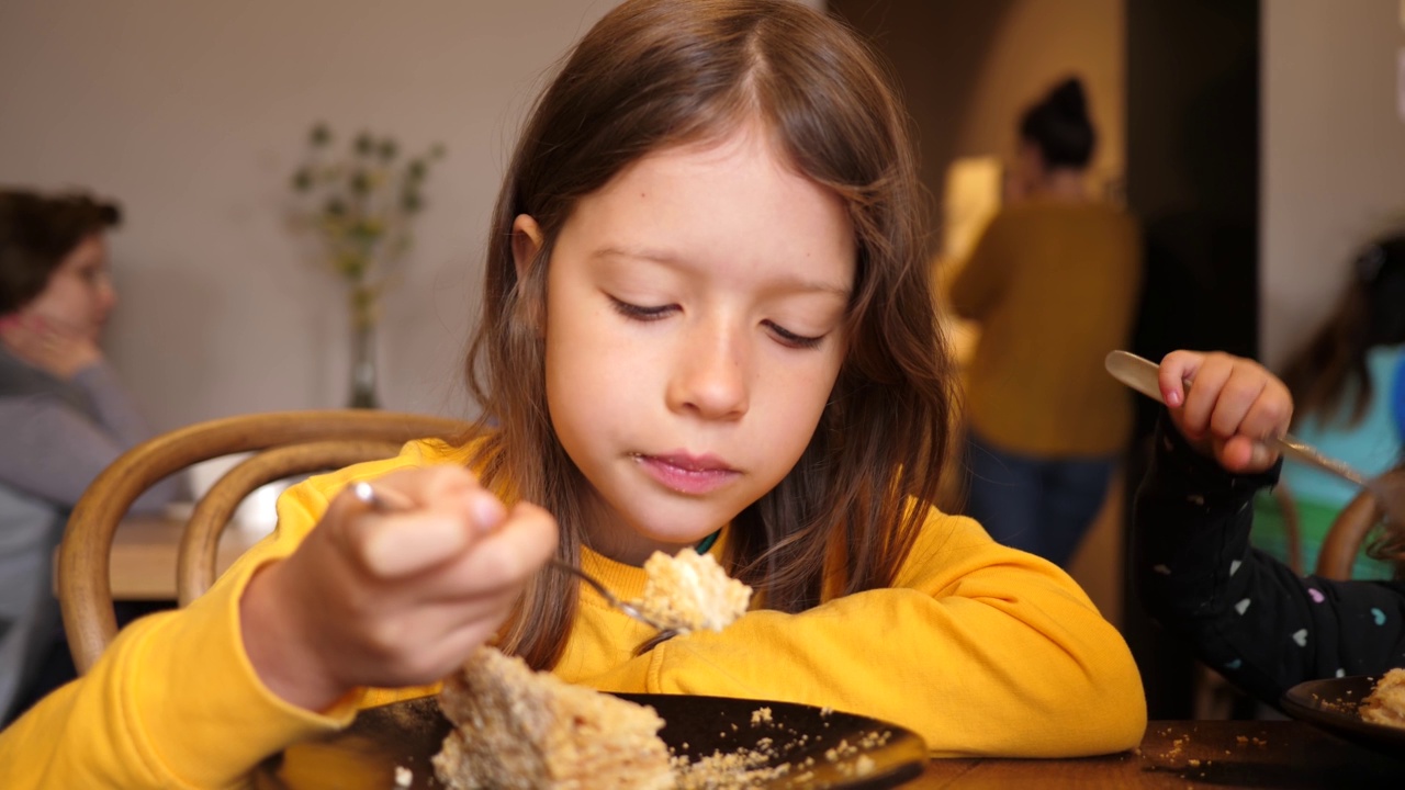 爱吃甜食的小女孩在室内的咖啡桌上用叉子吃美味的蛋糕视频素材