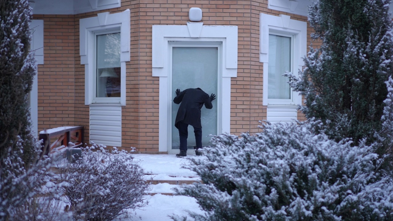 从外景镜头可以看到，窃贼正在雪地里的后院逃跑。一个白人年轻人，穿着黑色衣服，戴着滑雪面罩，在犯罪现场被抓。视频素材