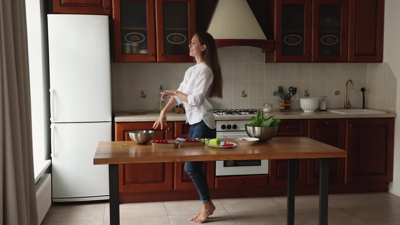 美丽的女人赤脚跳舞在舒适的厨房做饭视频素材