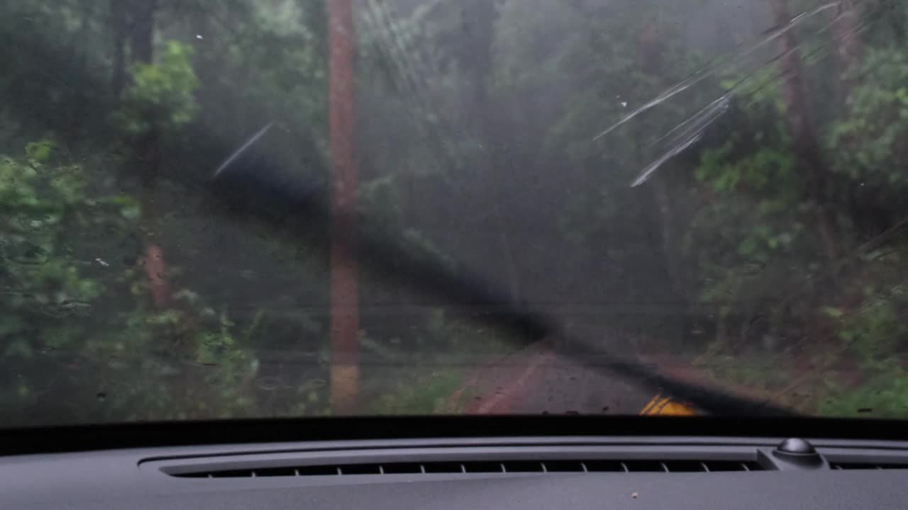 在雨中驾驶时，车内的雨点落在挡风玻璃上，雨刷也在工作。在一个下雨天，在森林里的路上开车。视频素材