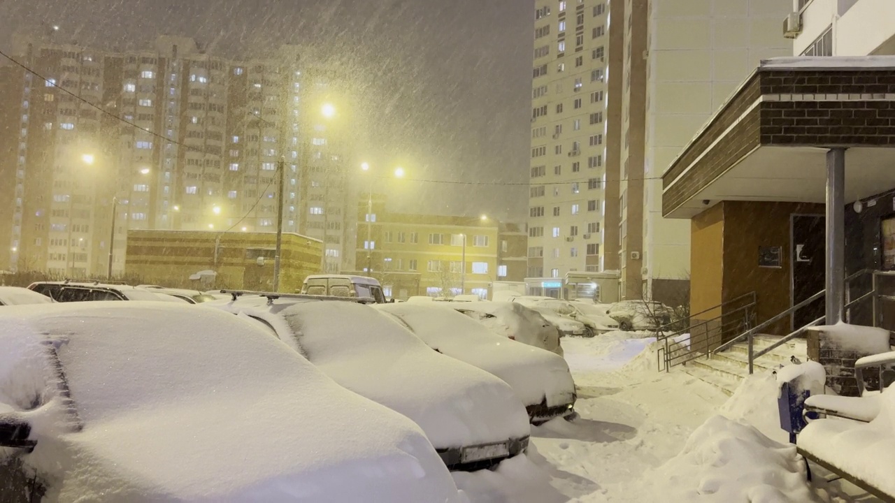 夜晚城市街道上大雪纷飞。冬天的城市。人行道和汽车完全被雪覆盖视频下载