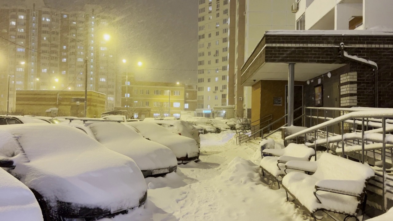 暴雪,暴风雪,风暴。夜晚城市街道上大雪纷飞。冬天在城市里。人行道和汽车完全被雪覆盖。视频下载