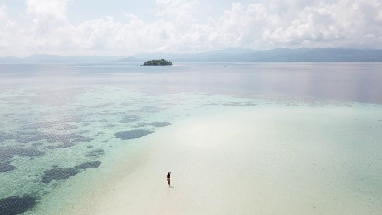 年轻的比基尼女子走在白色沙滩附近的蓝色热带海洋海浪。视频素材