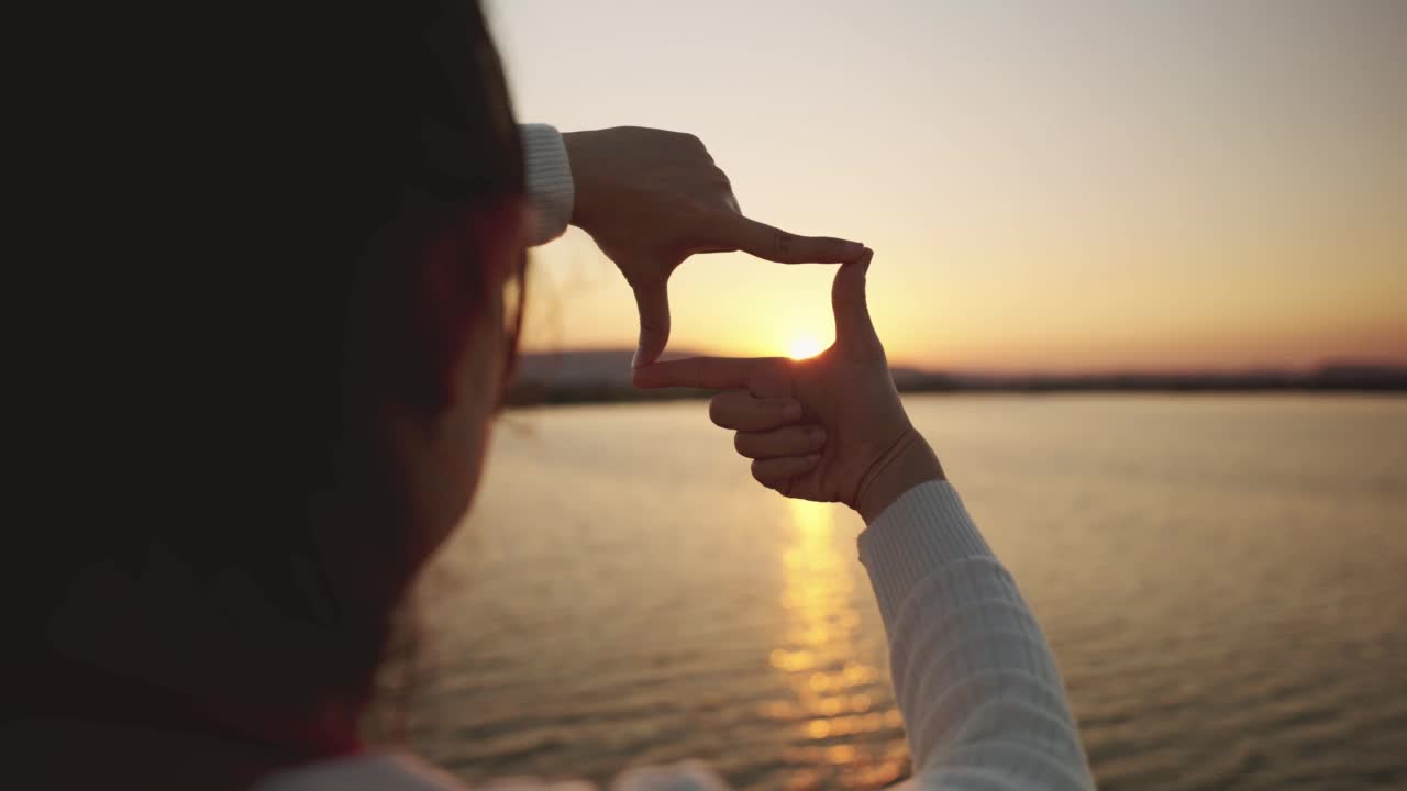 女人用手做夕阳的画框手势，新年计划和视觉概念，女人捕捉日出。视频素材