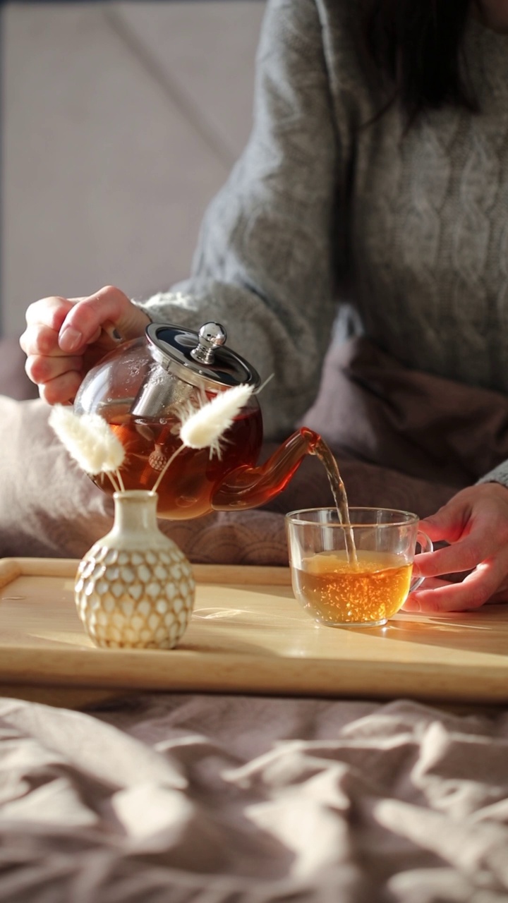 女人从玻璃茶壶中倒茶。舒适的家，hygge风格的室内。早餐茶道。视频素材