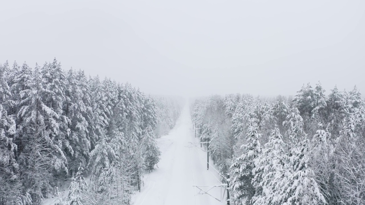 鸟瞰图无人机在冬季森林积雪覆盖的铁路轨道上飞行。林地下大雪。雪花纷纷落下。飞过白色的树林。暴风雪视频素材