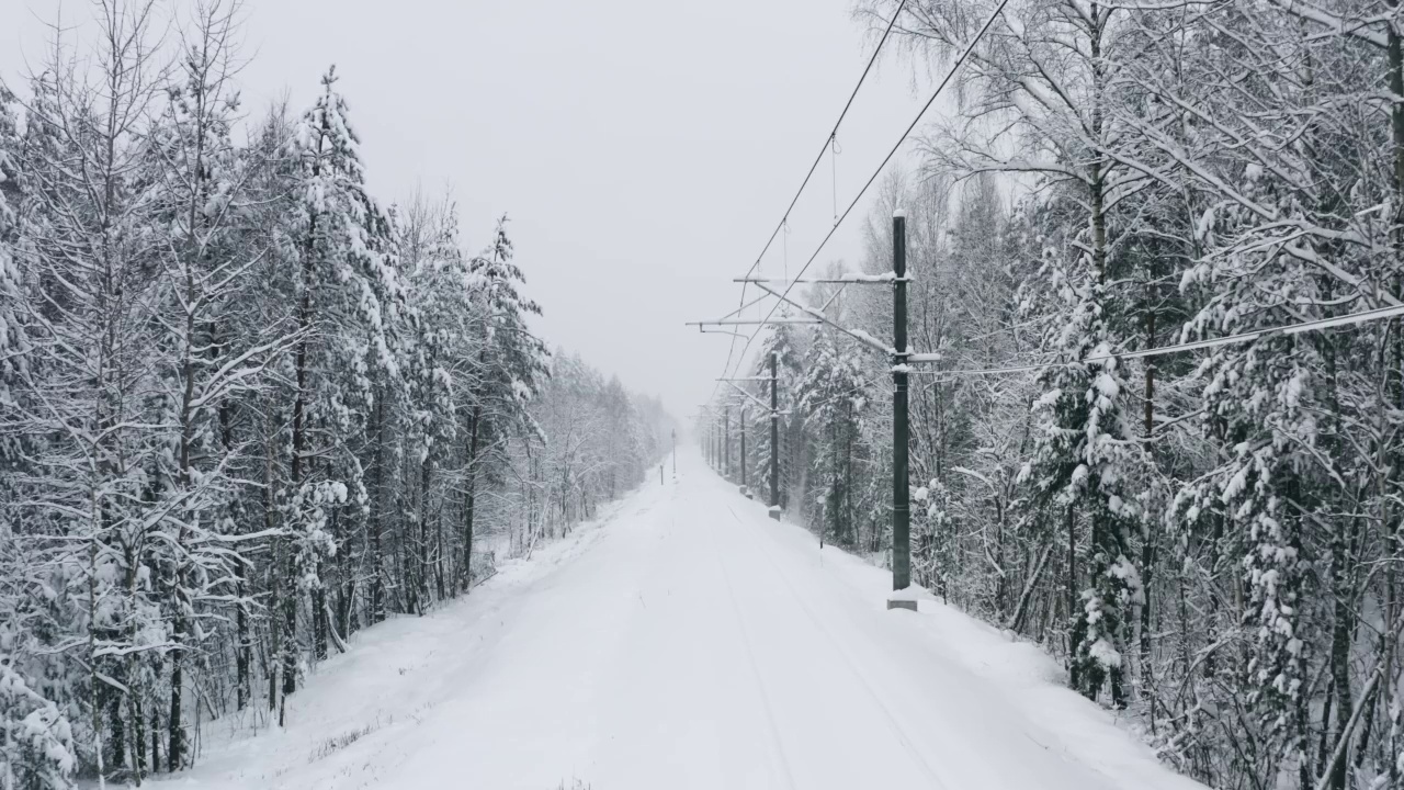 鸟瞰图无人机在冬季森林积雪覆盖的铁路轨道上飞行。林地下大雪。雪花纷纷落下。飞过白色的树林。暴风雪视频素材