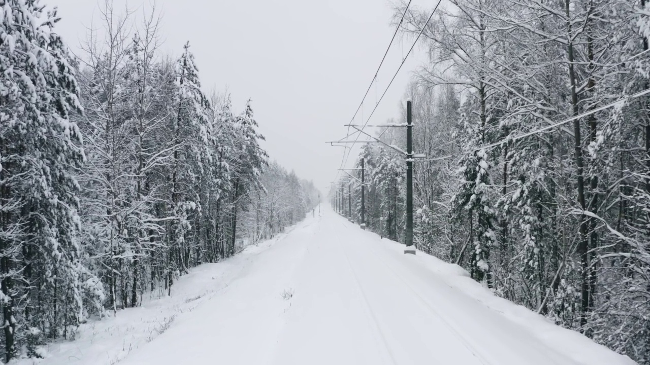 鸟瞰图无人机在冬季森林积雪覆盖的铁路轨道上飞行。林地下大雪。雪花纷纷落下。飞过白色的树林。暴风雪视频素材