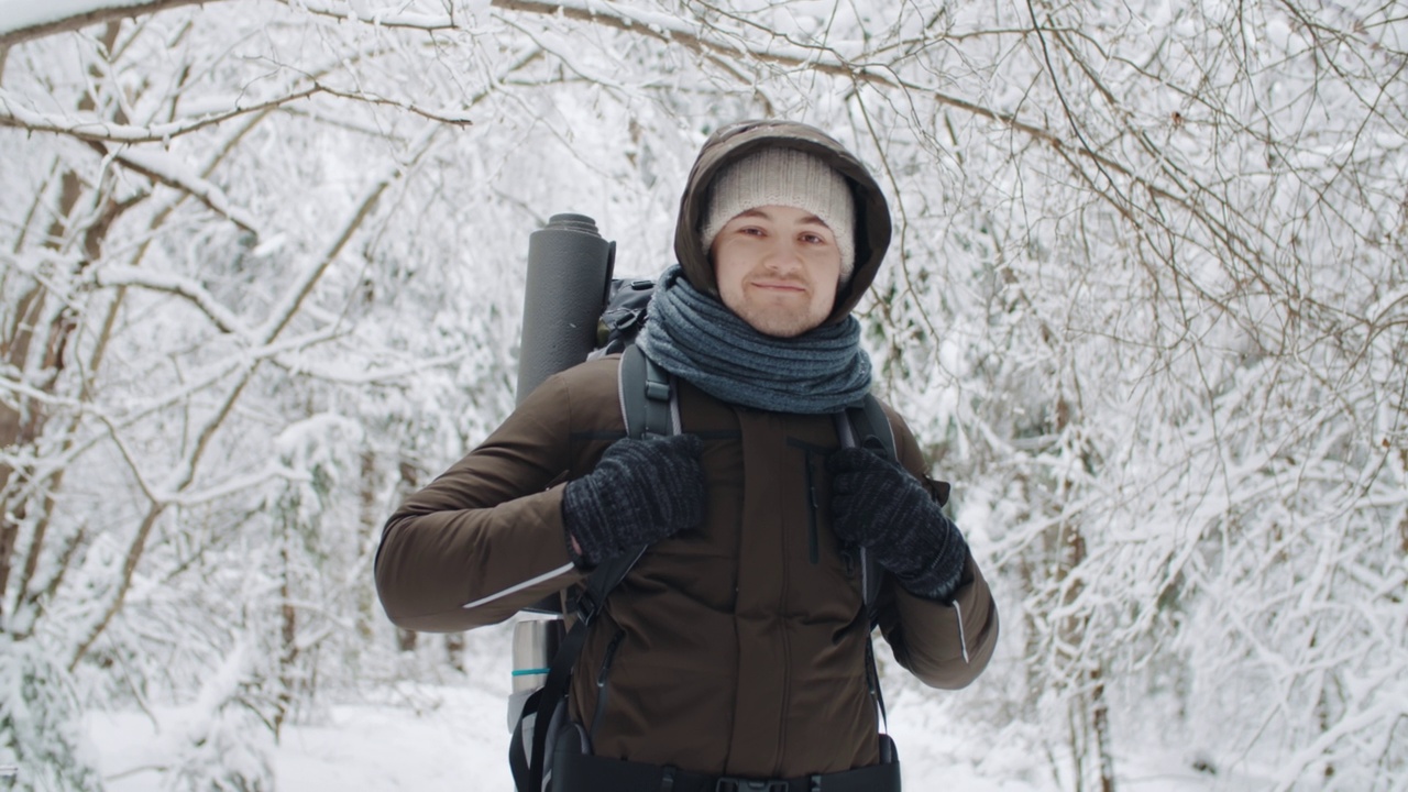 手持肖像年轻愉快的旅行者放松在冬季森林降雪。快乐的徒步旅行者看着镜头，微笑着享受在雪原森林里的徒步旅行。雪花。人与自然的概念视频素材