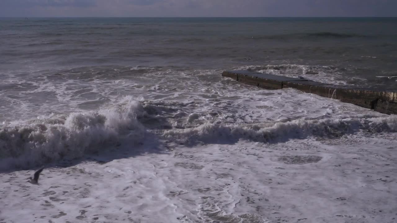 肮脏的风浪撞击着防波堤。风浪的泡沫漂浮在卵石滩上。视频下载