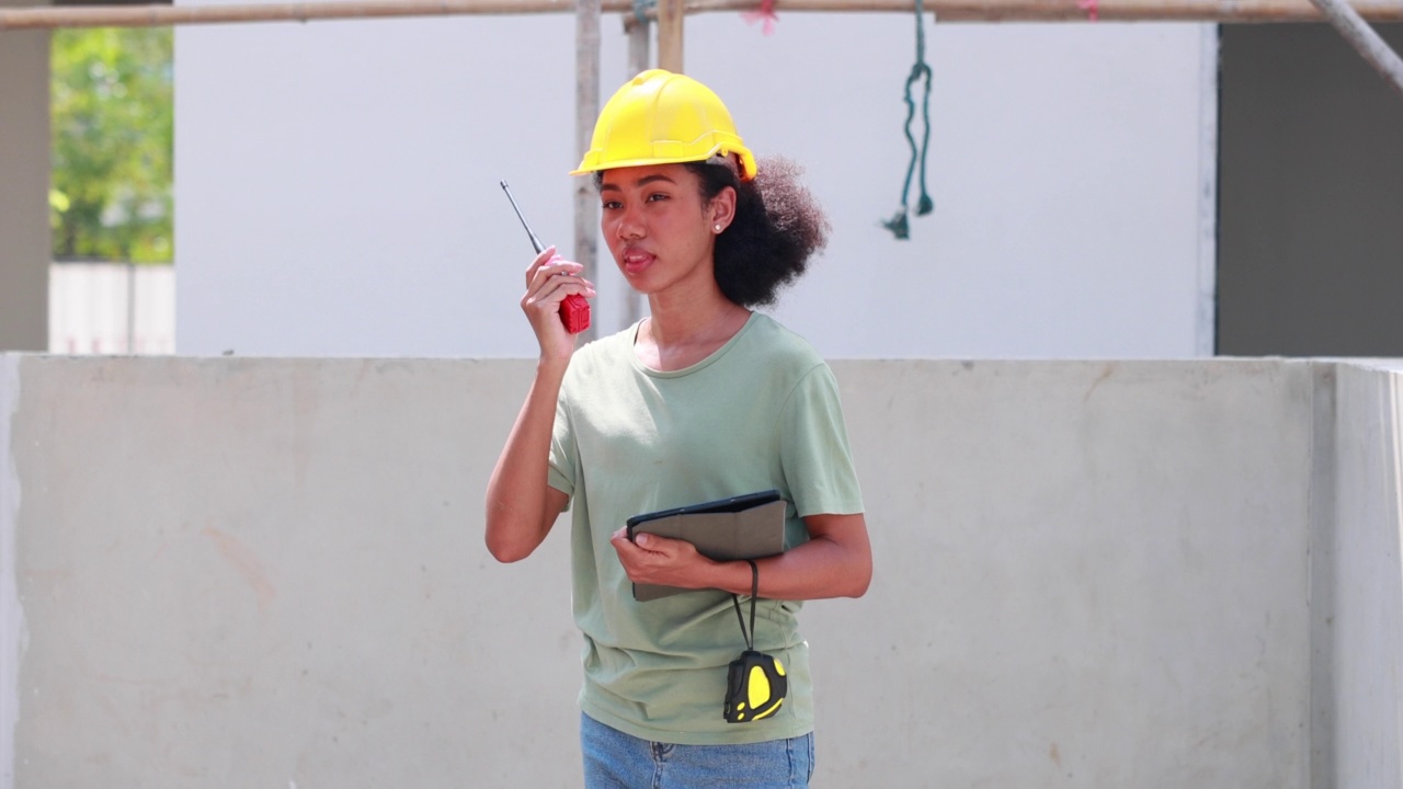 近距离面对黑人女性。非裔美国女性工程师工人戴着黄色安全帽在建筑工地工作。视频素材