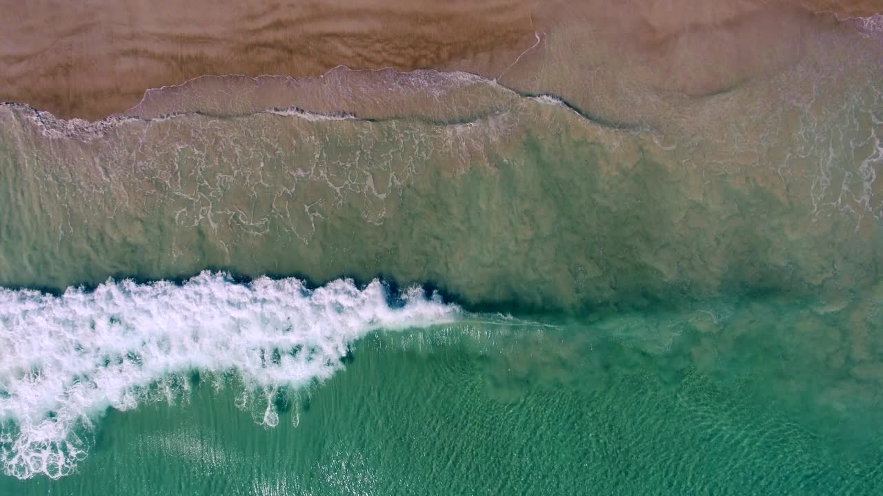 蓝绿色的海浪拍打着海岸的鸟瞰图，流畅的慢镜头视频素材