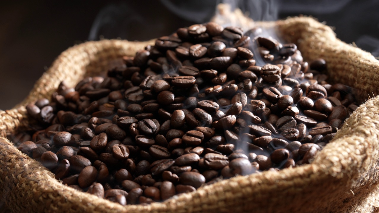 粗麻袋里的烤咖啡豆，上面有烟。新鲜烘焙的浓香深棕色咖啡豆，用粗麻袋熏制。缓慢的运动。视频素材