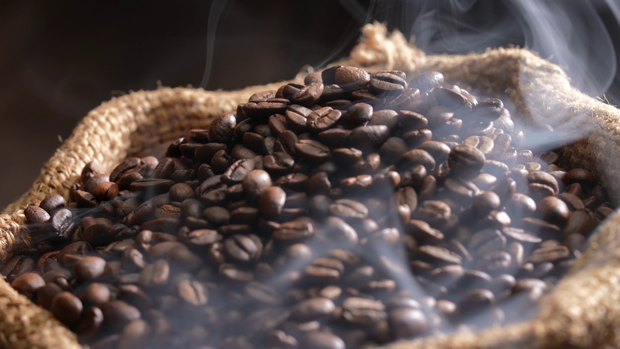 粗麻袋里的烤咖啡豆，上面有烟。新鲜烘焙的浓香深棕色咖啡豆，用粗麻袋熏制。缓慢的运动。视频素材