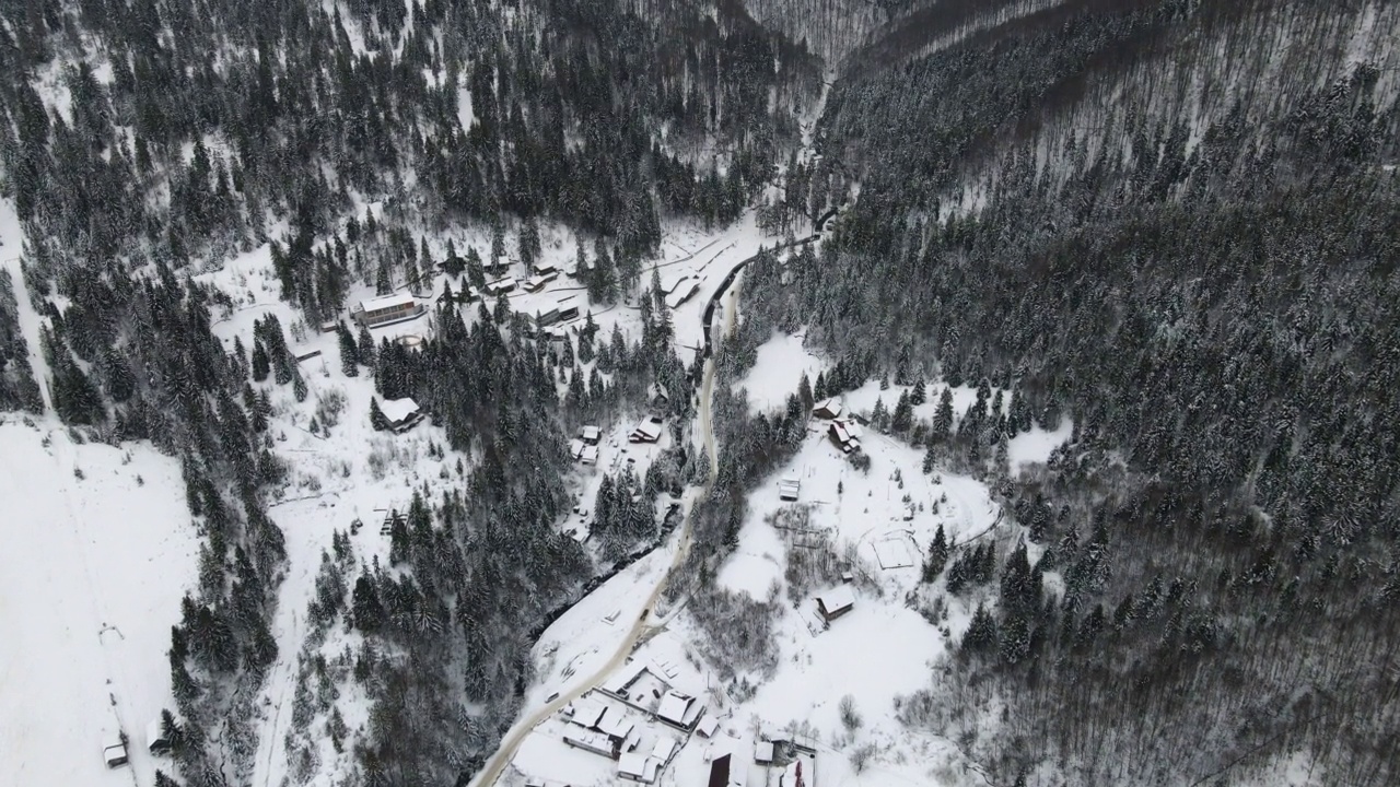 正在滑雪度假村上空飞行4K无人机。空中的冬季景观与小村庄的房子之间的积雪覆盖的森林在寒冷的山脉。视频素材