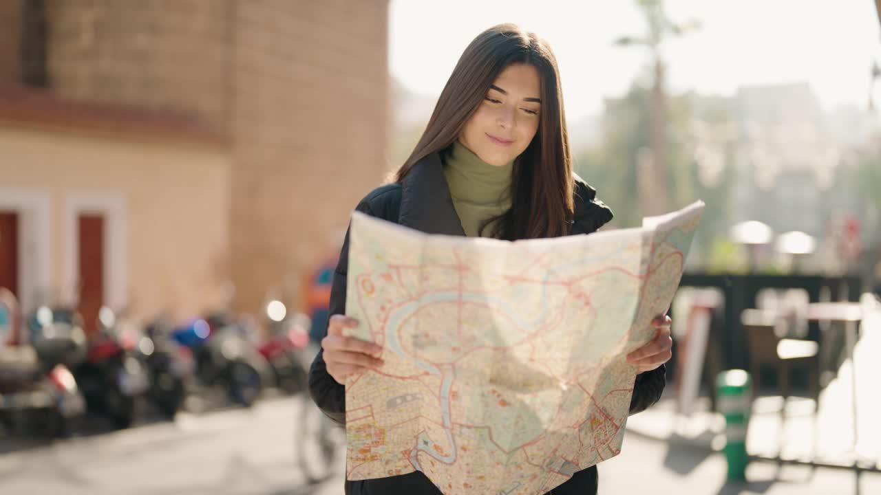 年轻的西班牙裔妇女微笑着自信地看在街上的城市地图视频素材