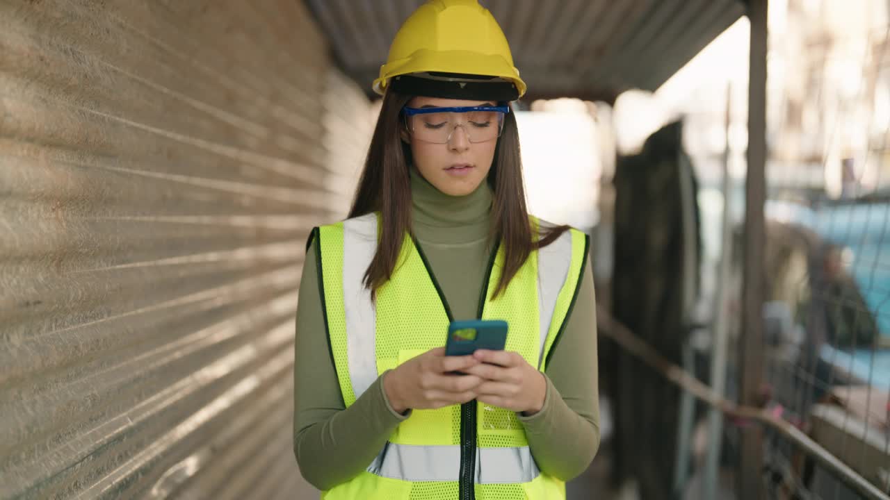 年轻的西班牙裔女建筑师在建筑工地使用智能手机视频素材