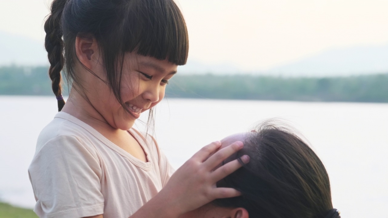 夕阳西下，母亲抱着可爱的小女儿在湖边散步。兴奋的小女孩笑着和妈妈在户外玩。母亲拥抱着女儿。视频素材