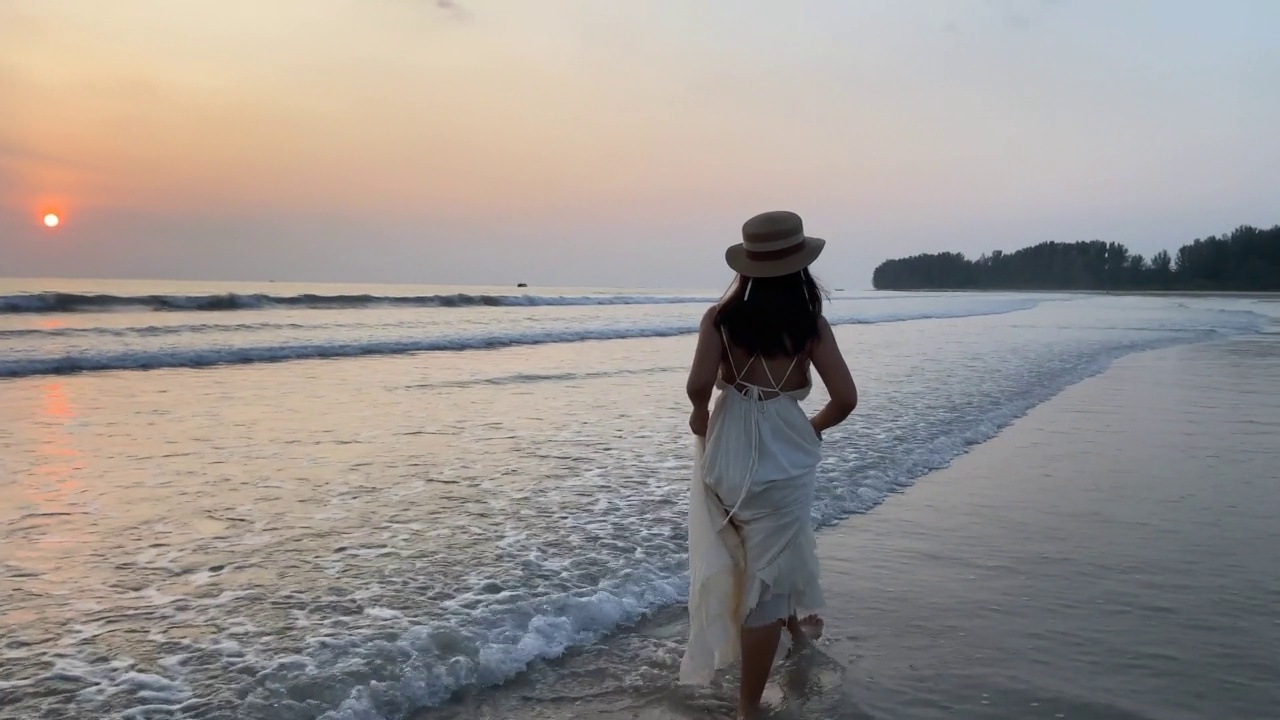 在泰国普吉岛的夏日度假中，身穿白色连衣裙的女子在美丽的夕阳下散步视频素材