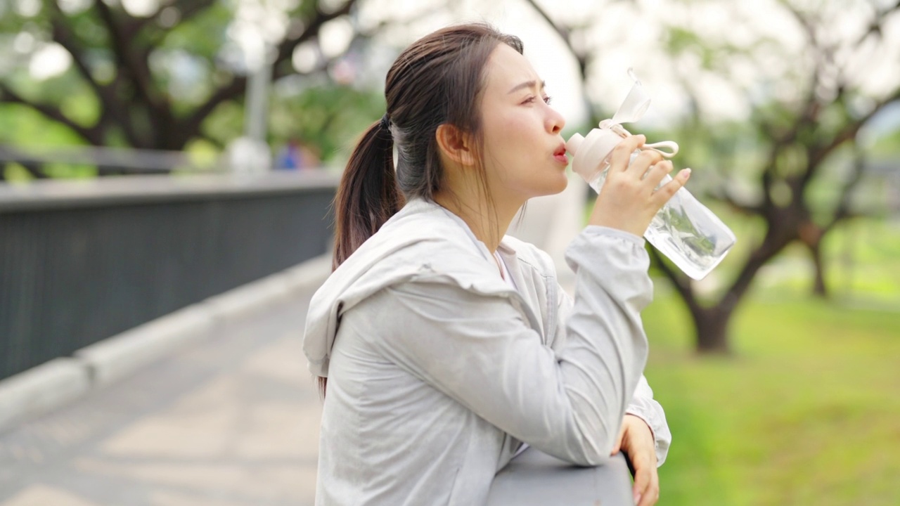 4K亚洲妇女早上在公园慢跑时喝瓶装水。视频素材