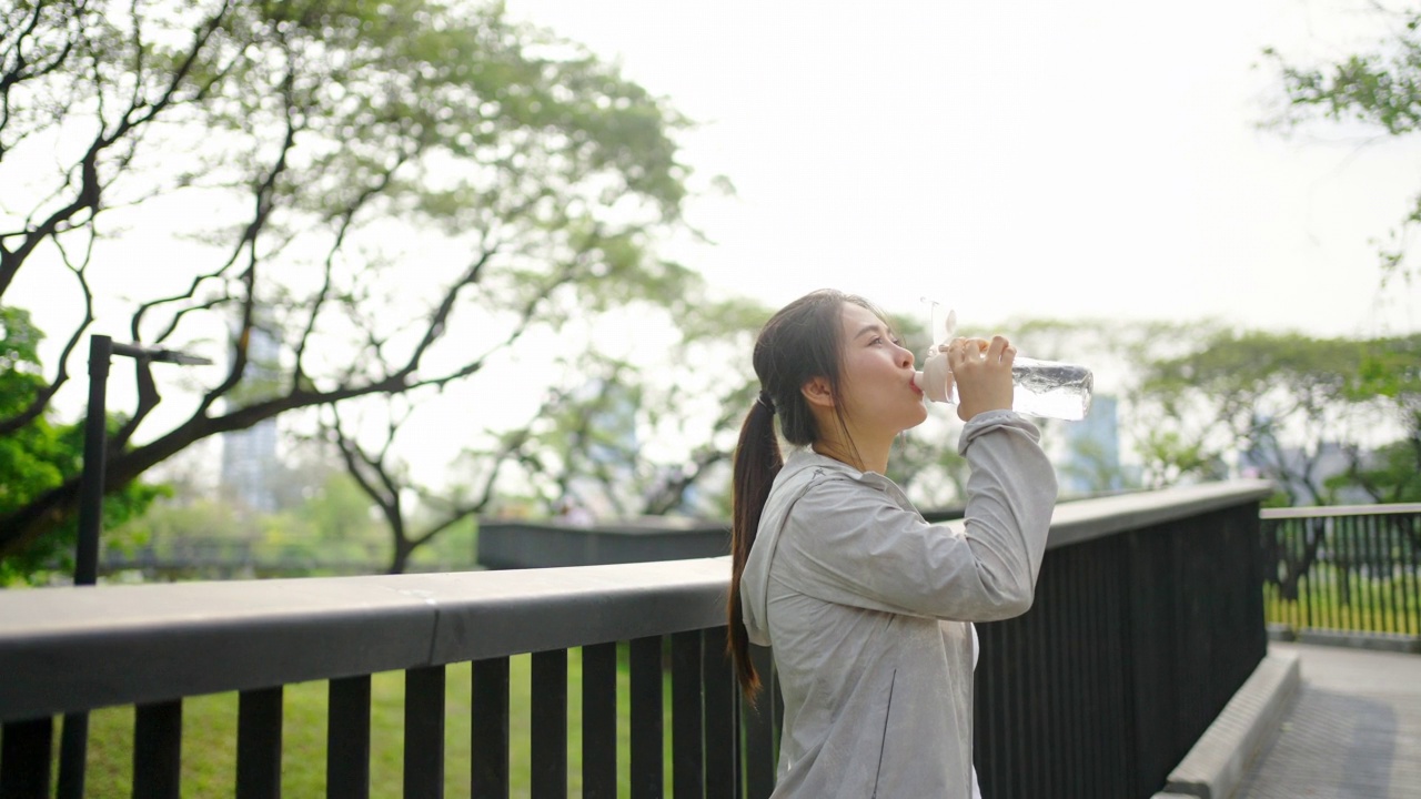 4K亚洲妇女早上在公园慢跑时喝瓶装水。视频素材