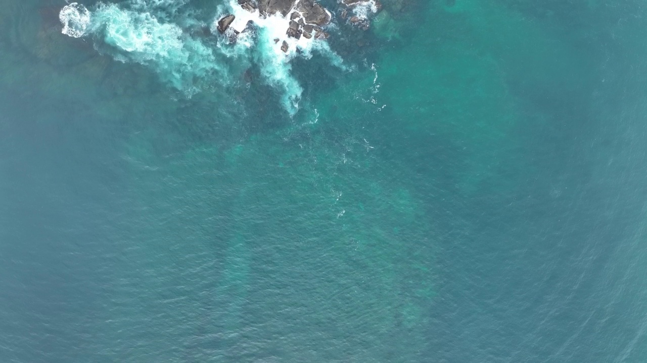 海浪撞击着海洋中的岩石。一幅宁静的自然景象。水中岩石的鸟瞰图。海洋与陆地的交汇处。慢动作120帧的视频视频素材