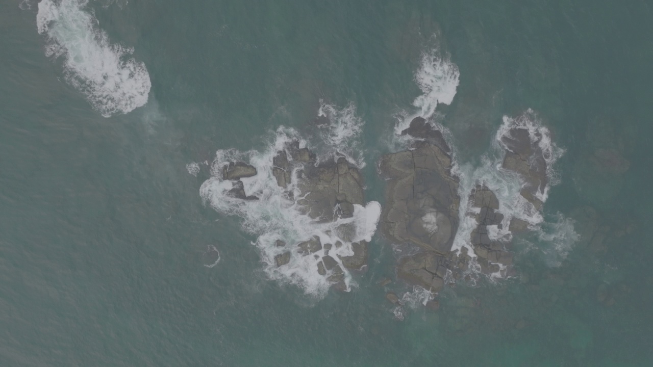 海浪撞击着海洋中的岩石。一幅宁静的自然景象。水中岩石的鸟瞰图。海洋与陆地的交汇处。120fps视频，ProRes, 10bit，未分级D-LOG视频素材