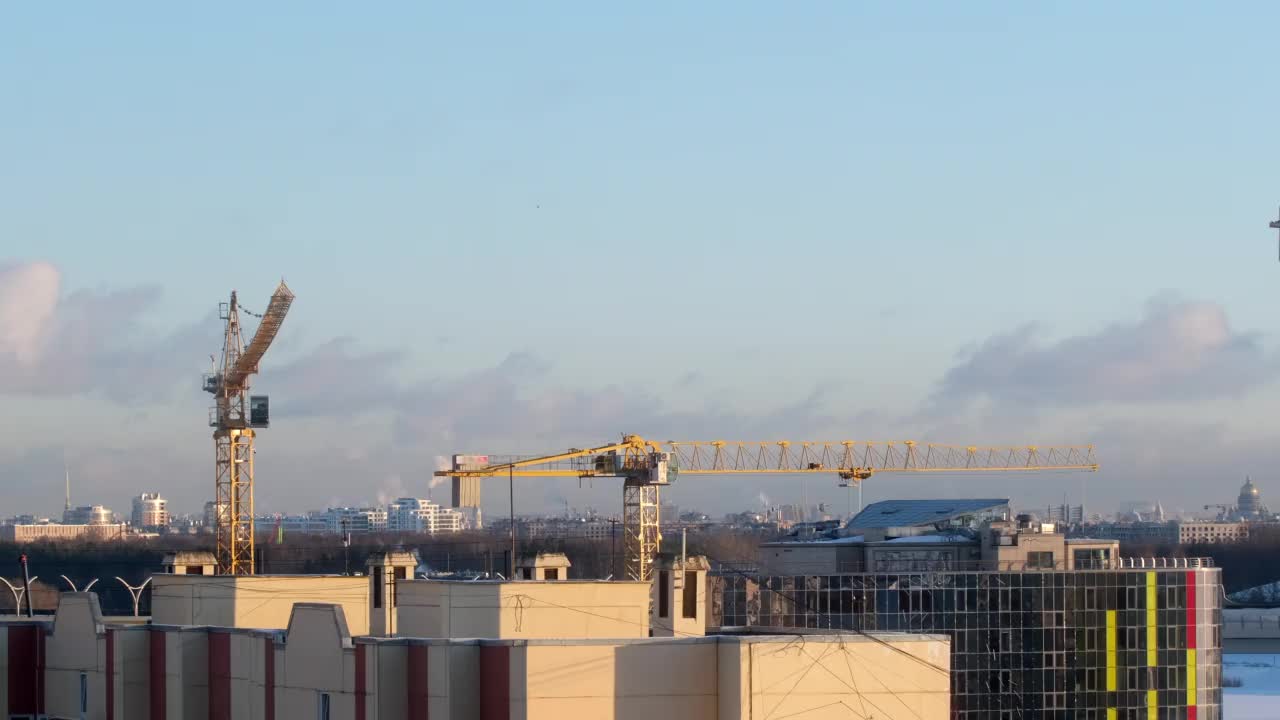 建筑工地上的起重机在城市和美丽天空的背景下吊起货物视频素材