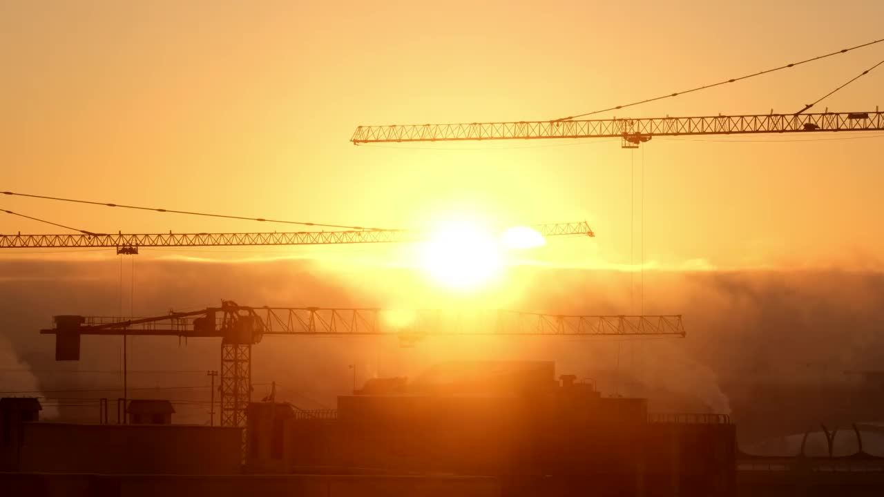 建筑工地上的起重机在雾和美丽天空的城市背景下举起货物视频素材