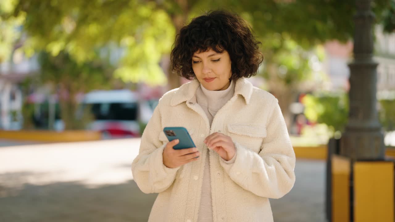 年轻的西班牙女性微笑自信地在公园用智能手机自拍视频素材