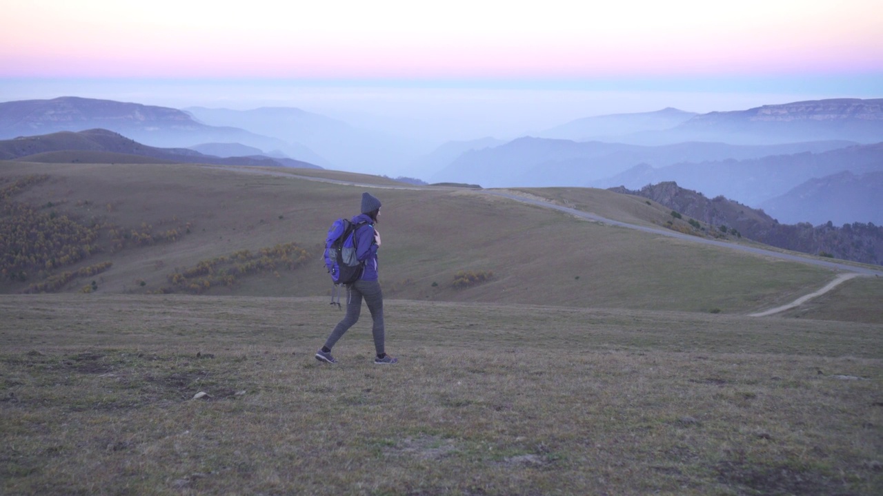 戴着帽子背着背包的女游客在美丽的群山中旅行视频素材